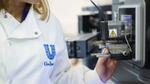 Nahaufnahme eines Wissenschaftlers in einem weißen Laborkittel mit dem Logo von Unilever, der durch ein großes digitales Mikroskop schaut.